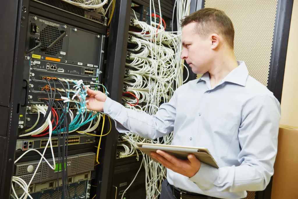 Network monitoring engineer inspecting switches, cabling and network infrastructure in a server rack.