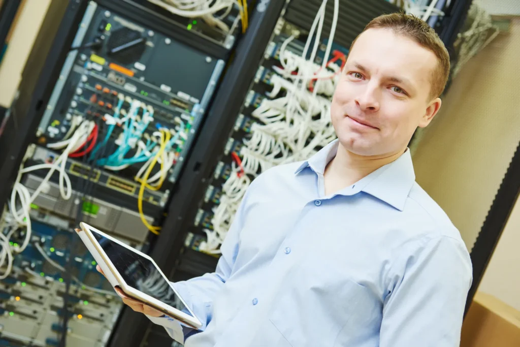 Network monitoring engineer reviewing business routers, switches and network infrastructure in a server room.